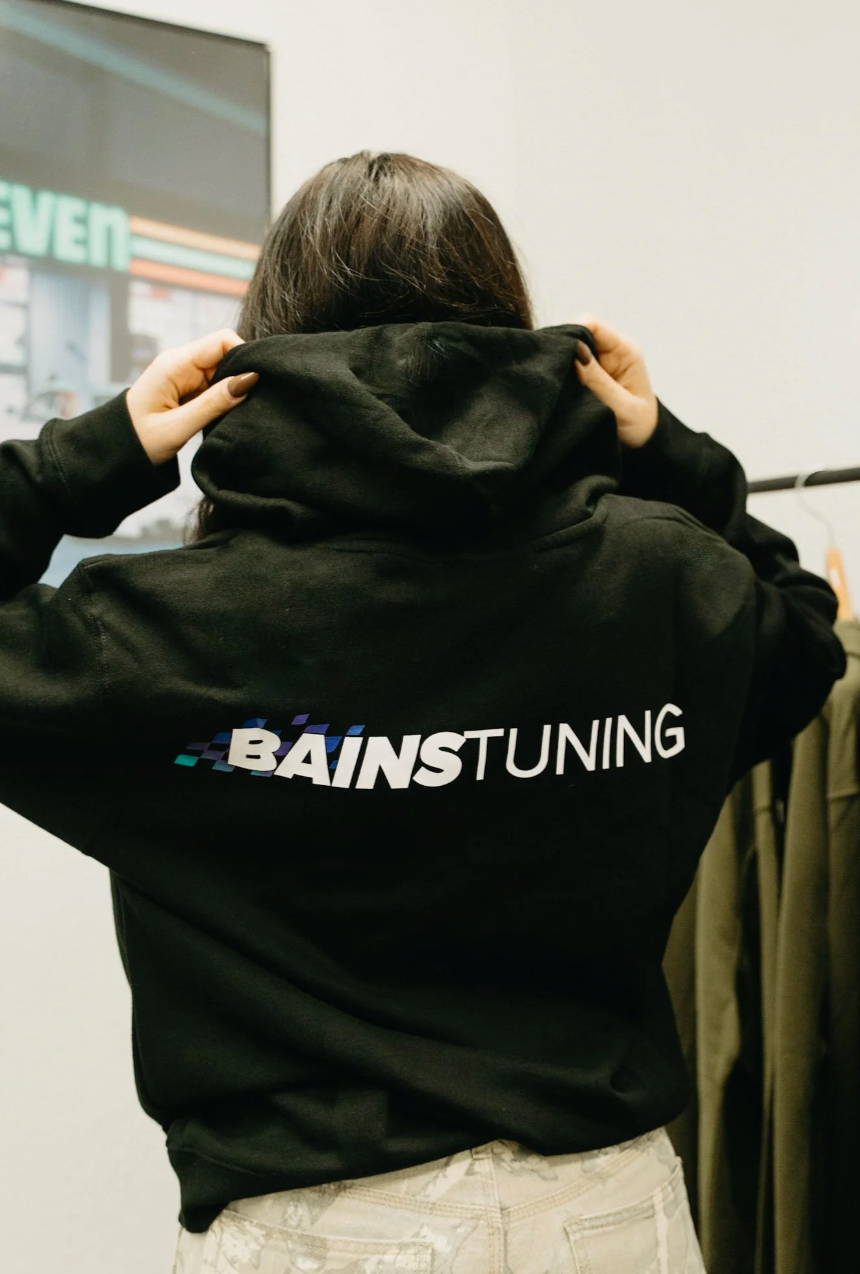 Person wearing a black hoodie with 'Bains Tuning' text, standing indoors.